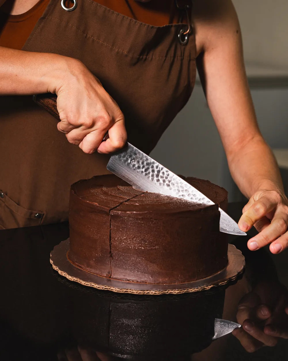 Manos rebanando un pastel de chocolate entero
