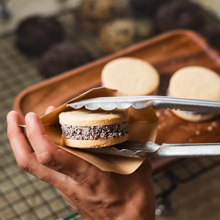 Alfajor tomado con pinzas y puesto en su sobre de papel
