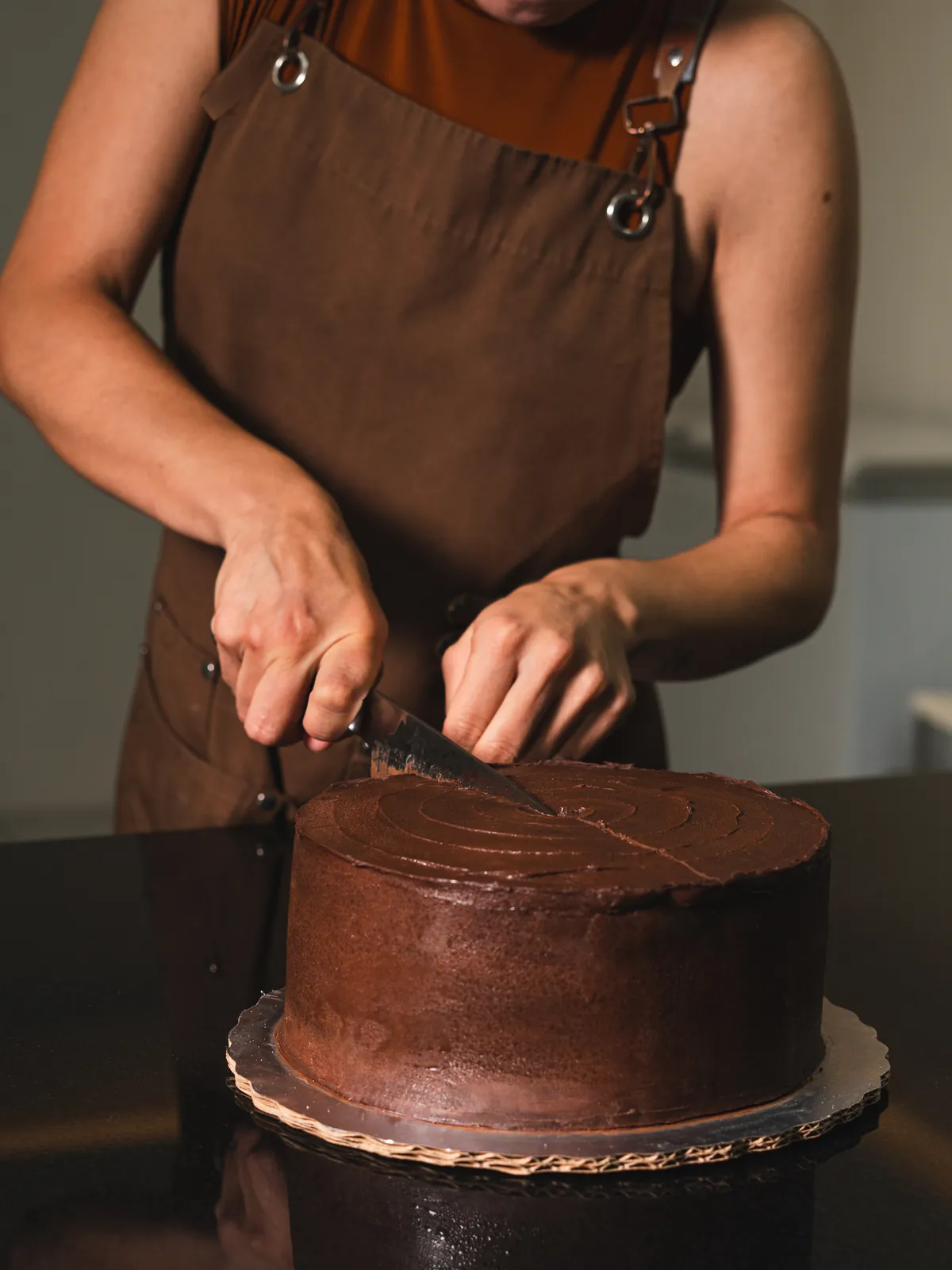 Manos rebanando un pastel de chocolate entero en el obrador de Lari's Bakehouse