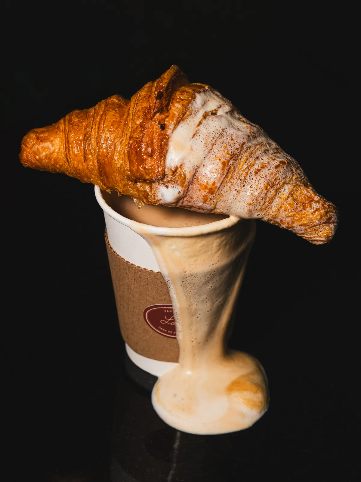 Croissant recién horneado sobre un vaso de café para llevar