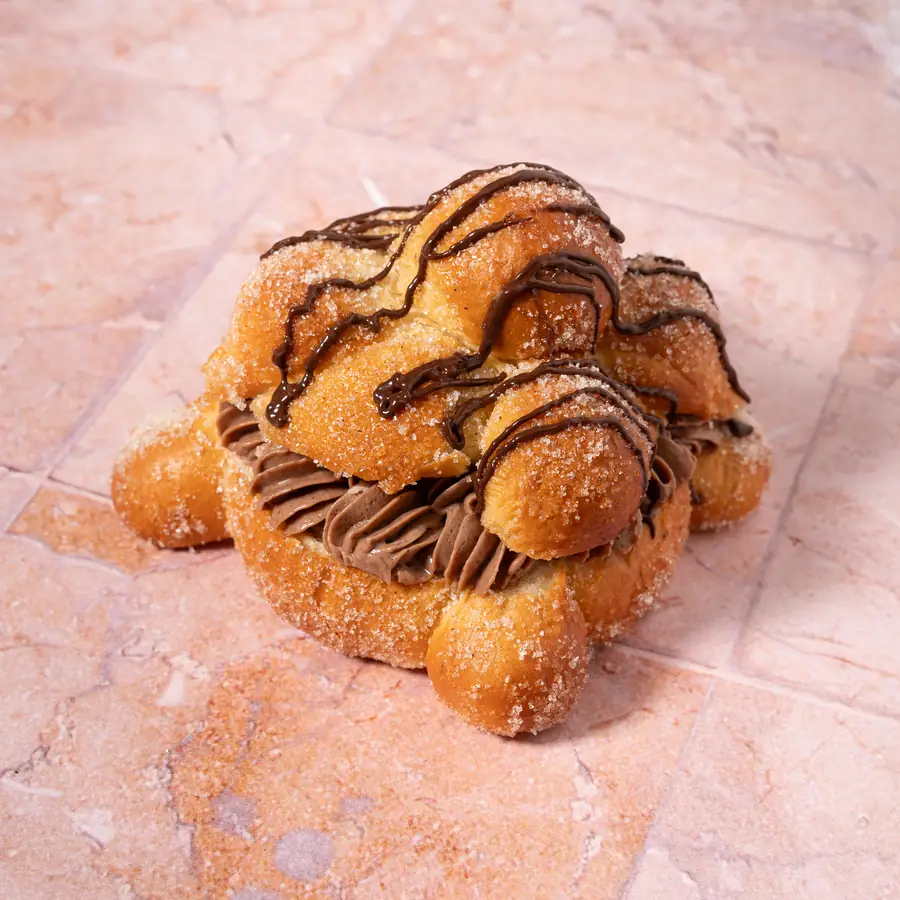 Pan de muerto con relleno y hilos de chocolate sobre loseta rosa